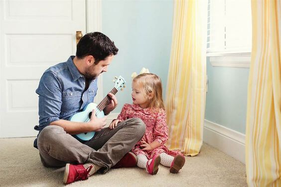 Rapporto padre-figlia: il padre suona la chitarra e la bimba canta.