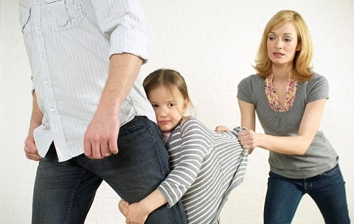 Una bambina fa i capricci attaccandosi alla gamba del padre.