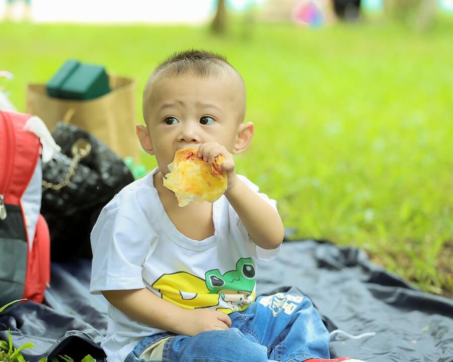 Bambino mangia una pizza: non è sempre consigliata come alimentazione dei bambini fino a 3 anni.