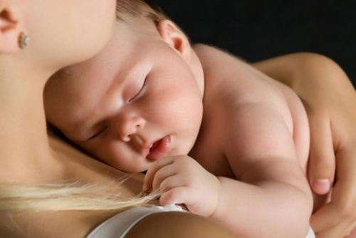 Un neonato dorme in braccio alla madre.