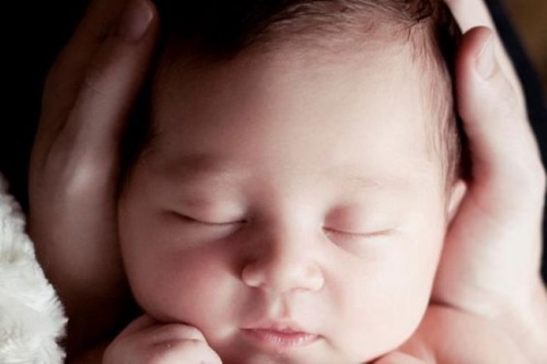 Anche i neonati sognano: un piccolo ad occhi chiusi con la testa tra le mani della mamma.