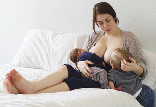 Donna sul letto che dà il seno a entrambi i figli