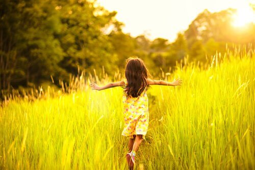 Bambina che corre in un prato con le braccia aperte