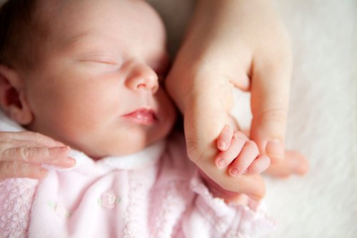 Neonata che tiene la mano della mamma mentre dorme