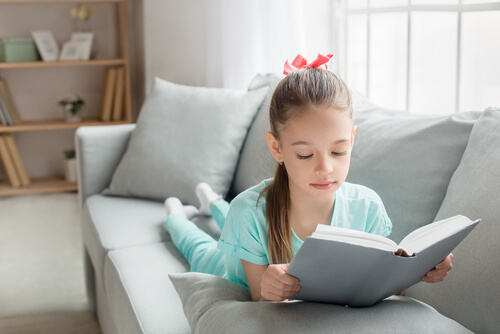 Bambina che legge un libro sul divano