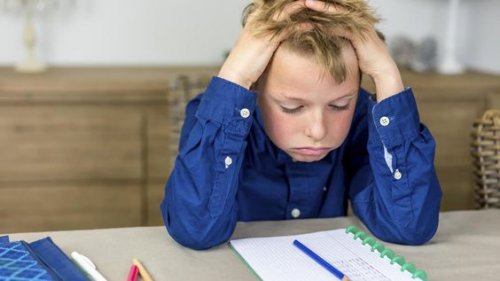 Bambino si mette le mani nei capelli mentre fa i compiti