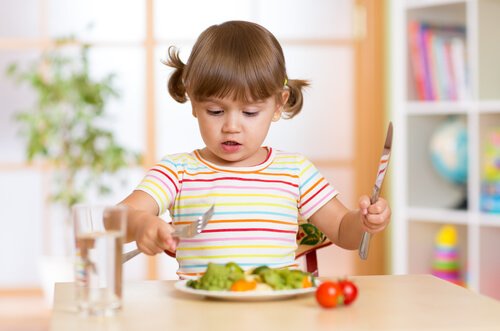 Bambina mangia con le posate un piatto di verdure