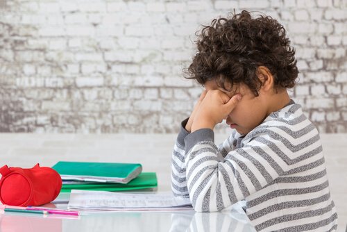 bambino con gomiti su tavolo e pugni su occhi