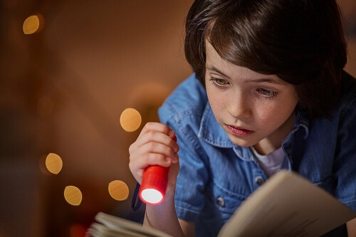 bambino legge libro con torcia