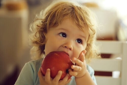 bimba addenta mela rossa tenuta con le mani