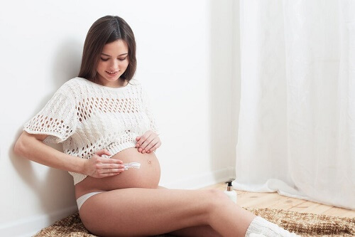 donna incinta seduta accanto a muro mette crema su pancione