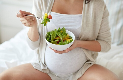 donna incinta seduta su letto mangia insalata