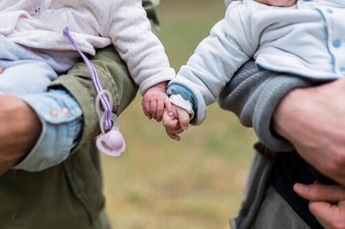 due neonati tenuti in braccio si toccano le mani