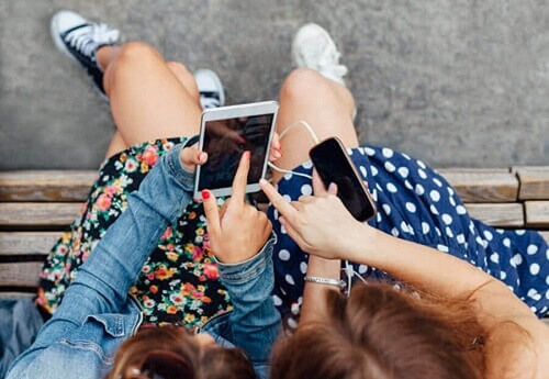 due ragazzine su una panchina giocano con i loro smartphones