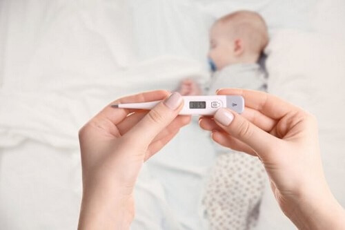 madre sostiene termometro con neonato sul letto