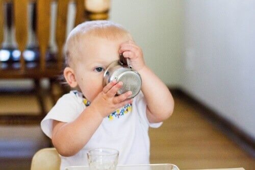 piccola bimba beve da una tazza di metallo