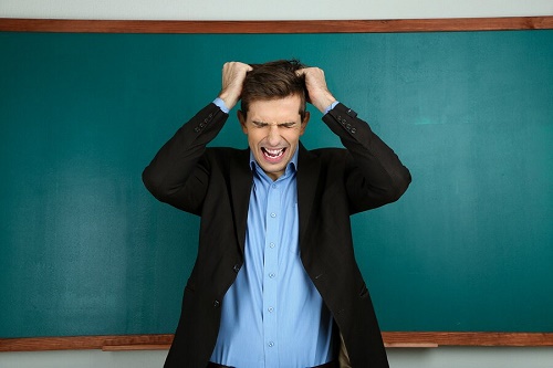 uomo si strappa i capelli davanti lavagna