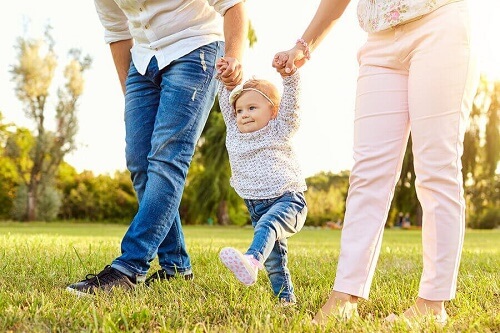 Bambina cammina tenuta dai genitori