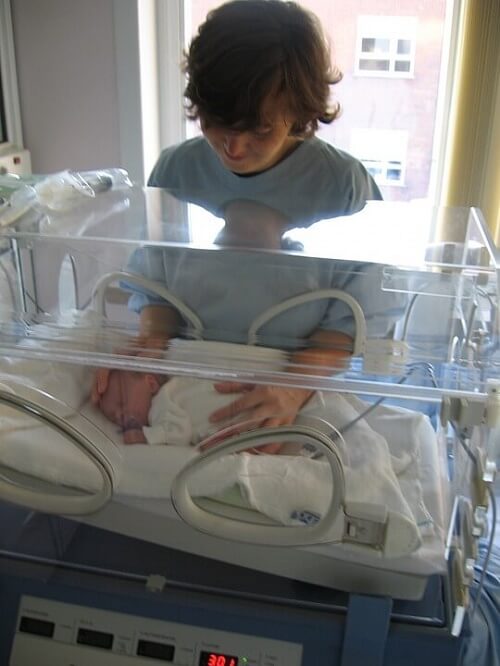 Fratellino accarezza neonato prematuro dentro un'incubatrice