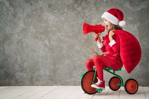 Frasi natalizie per i più piccoli: bambina sul triciclo vestita da babbo natale.