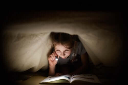 Bambina che legge sotto le coperte con la torcia