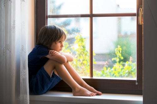 Bambino triste guarda fuori dalla finestra.