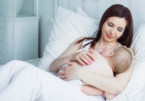 I grassi del latte materno e la crescita del neonato. Mamma che allatta in un letto bianco.