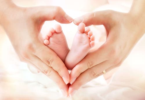 Mamma con mani a cuore sui piedini del bambino