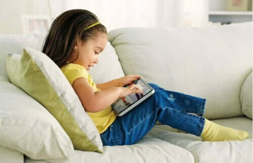 Bambina seduta sul divano che usa un tablet per giocare.