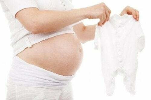 Donna incinta mostra un vestitino da bebè: come sapere se sei pronta a diventare mamma.