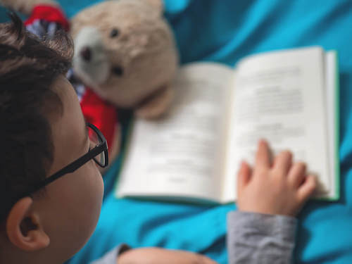 Bambino con gli occhiali che legge un libro.