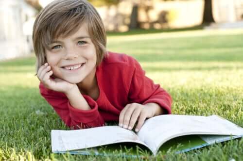 Bambino sorridente che legge un libro in un parco.