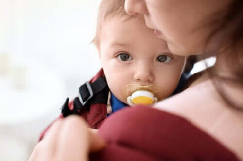 Bambino in braccio alla mamma col ciuccio in bocca.