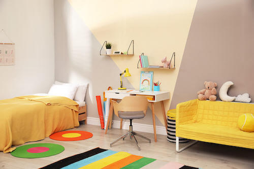 Cameretta del bambino con letto, scrivania e divano giallo.