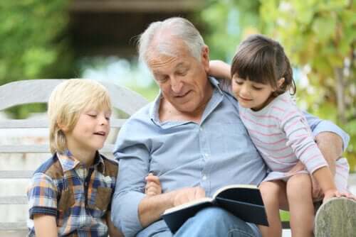 Nonno seduto su una panchina che legge un libro di Gianni Rodari ai nipoti.
