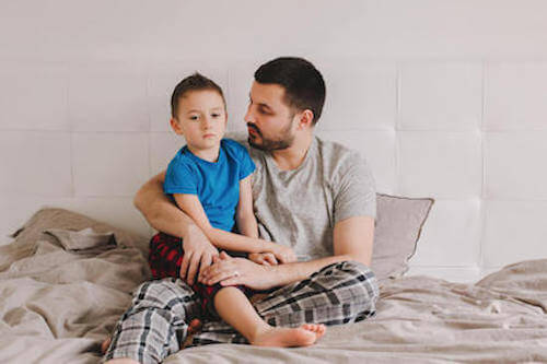 Padre seduto sul letto che tiene in braccio il figlio.