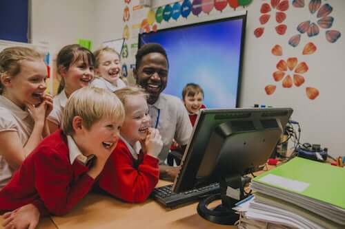 Insegnante ed alunni che ridono e fanno lezione davanti ad un computer.