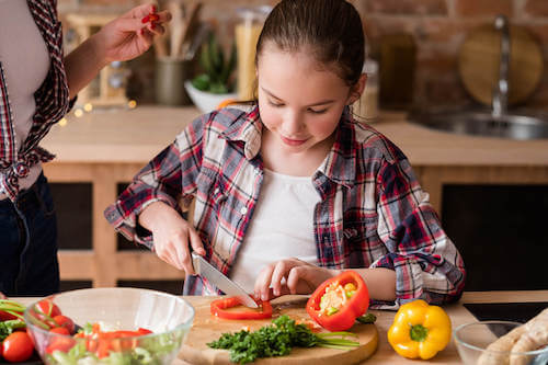 Bambina vegana che taglia le verdure per preparare un'insalata.