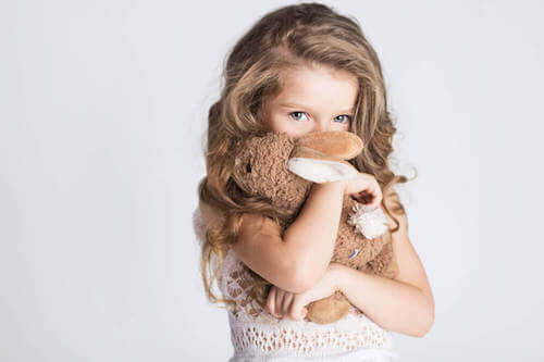 Bambina timida che si nasconde dietro un coniglio di peluche.