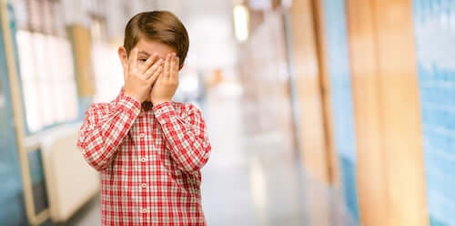 Bambino timido che si nasconde la faccia con le mani.