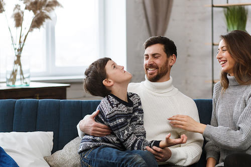 Padre, madre e figlio che giocano e ridono seduti sul divano.