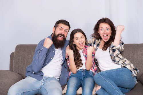 Padre, madre e figlia che si divertono seduti sul divano.