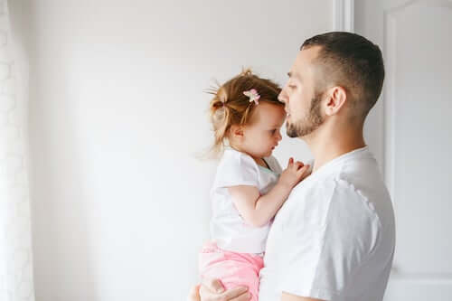 Padre che tiene in braccio la figlia neonata e le dà un bacio.
