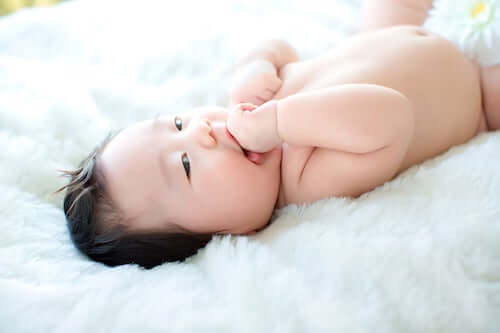 Neonato sdraiato sul letto che si succhia il dito.