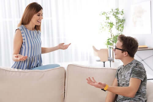 Madre che parla e scherza con il figlio adolescente seduto sul divano.