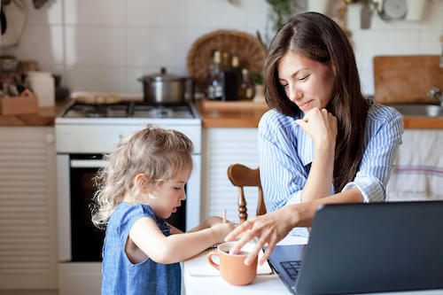 Madre che prende un caffè in cucina e guarda la figlia che fa un disegno.