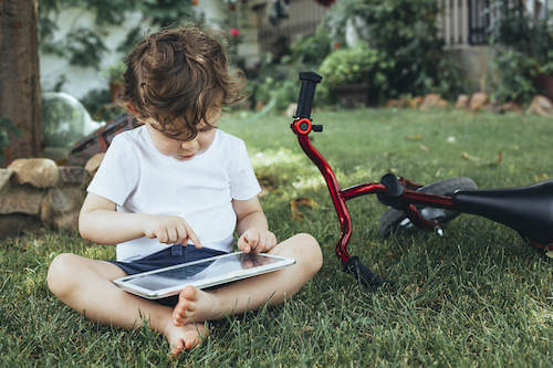 Bambino seduto sul prato del giardino di casa che usa il tablet.