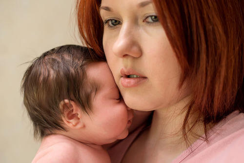 Donna triste e pensierosa che tiene in braccio il figlio neonato.