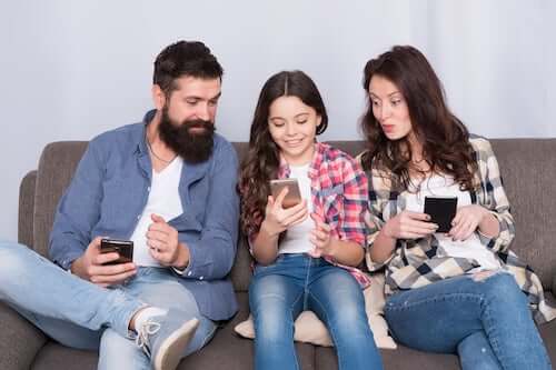 Padre e madre che navigano su internet insieme alla figlia usando il telefono.