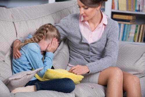 Bambina che piange sul divano con sua madre che la conforta.
